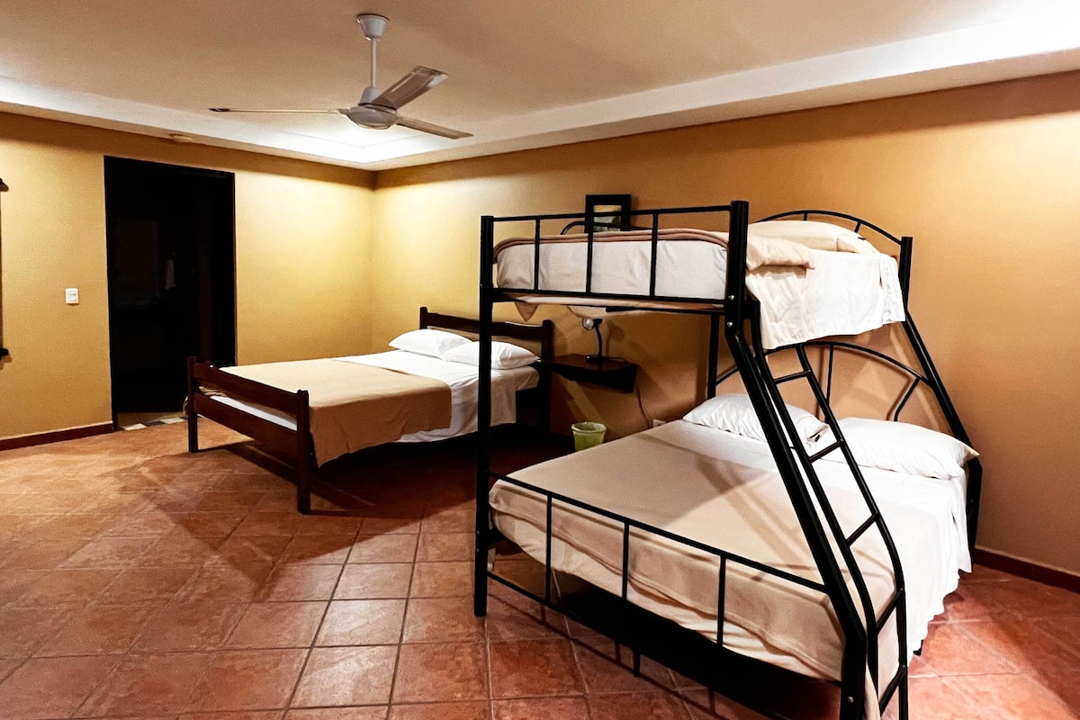 A room with two bunk beds, a single bed, a ceiling fan, and a tiled floor.