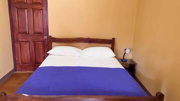 Una cama individual con estructura de madera, ropa de cama blanca y una manta azul.