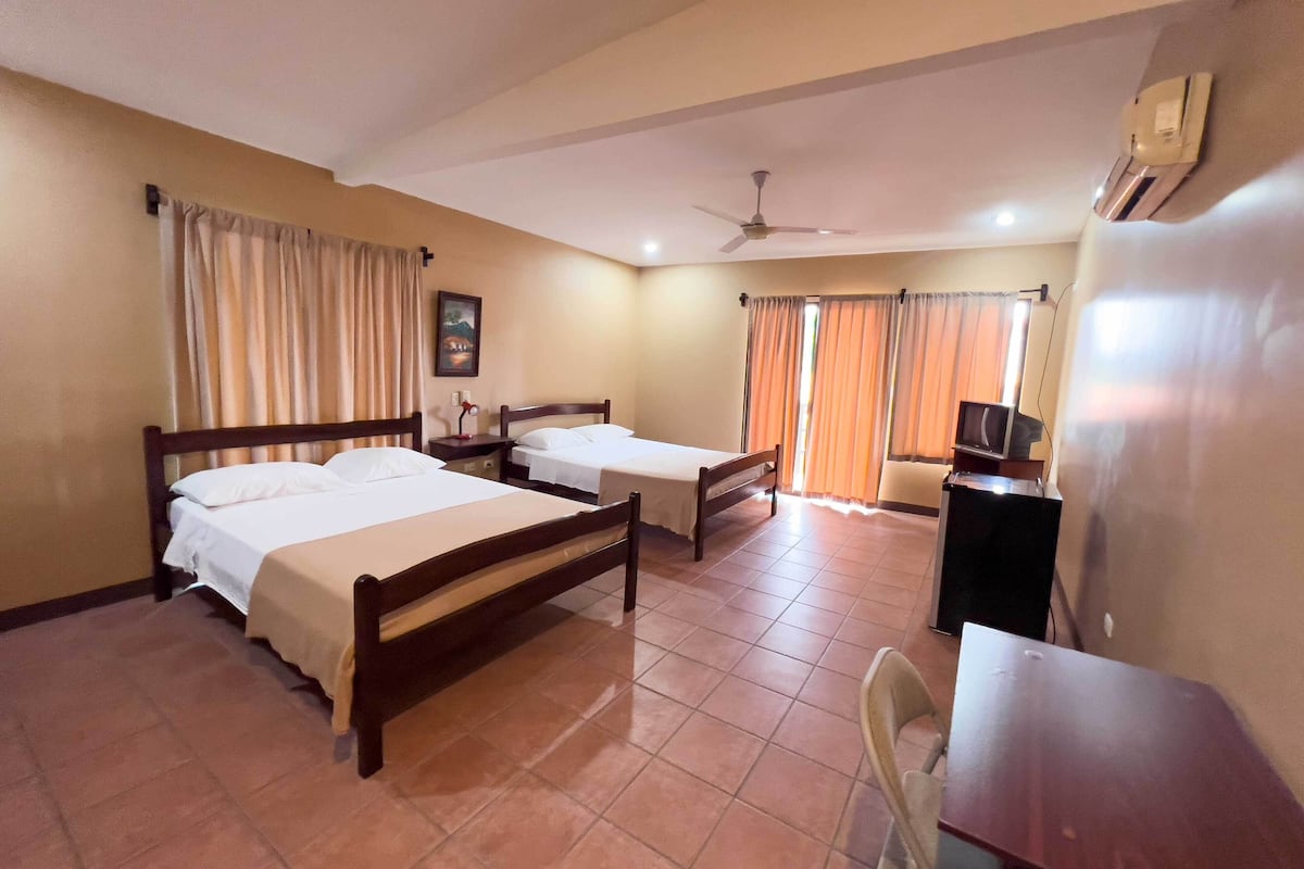 A hotel room with two beds, a desk, a chair, a ceiling fan, and a TV.