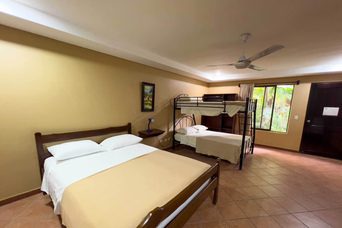 A hotel room with a bunk bed, a single bed, a ceiling fan, a window with curtains, and a door.
