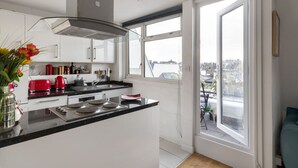A modern kitchen with a central island, white cabinetry, and a large window offering a view of the city.