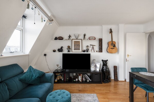 Una sala de estar con un sofá azul verdoso, una mesa de centro, un televisor sobre un soporte negro y una guitarra en la pared.