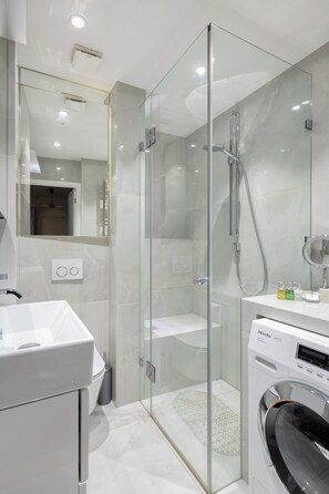 Un baño moderno con ducha acristalada, lavabo integrado y lavadora de carga frontal.