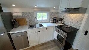 A modern kitchen with white cabinets, a stainless steel dishwasher, a double sink, a gas stove, and a window providing natural light.
