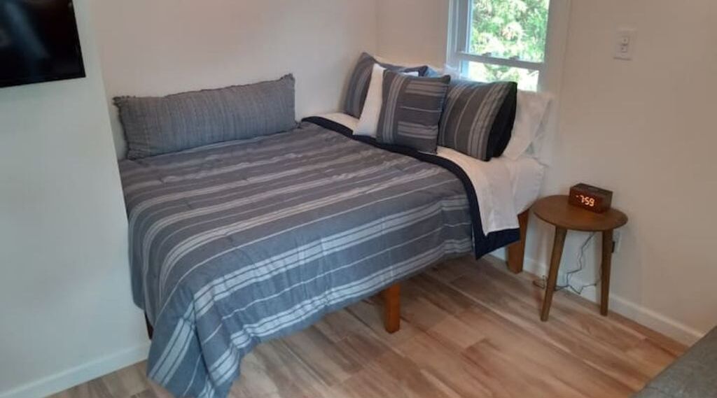 A bedroom with a bed, pillows, a small table, and a window.