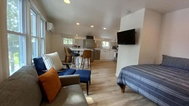A spacious living area with a sofa, chairs, a television, and a kitchen in the background.