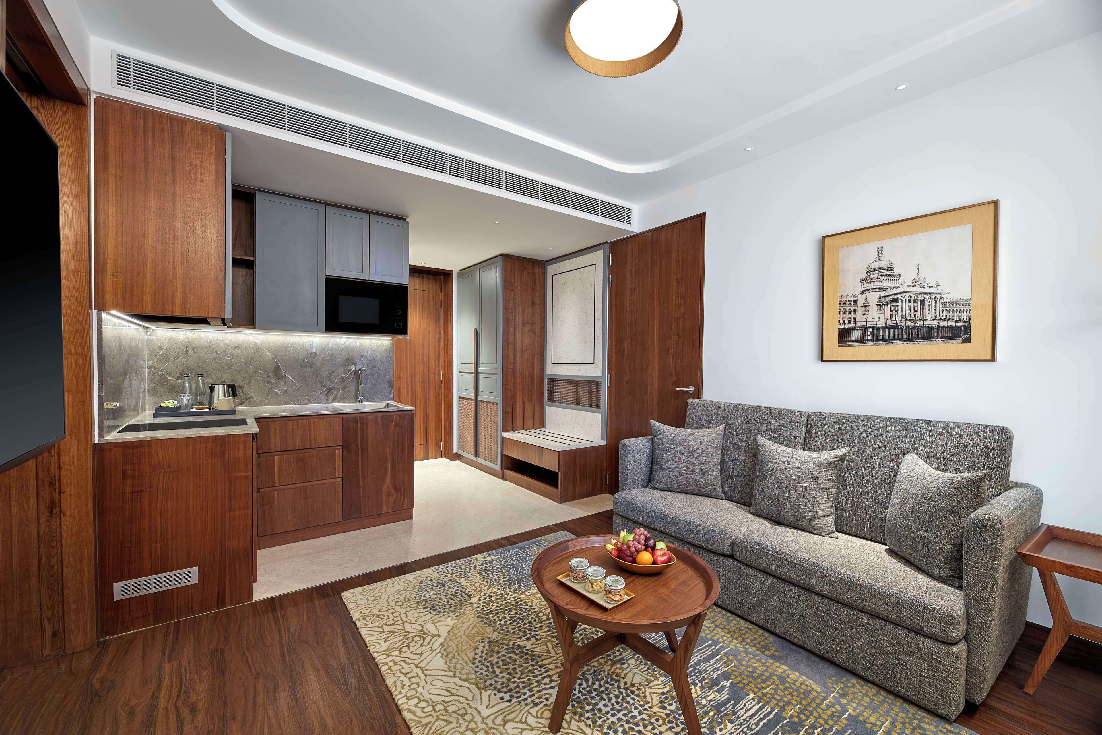 A modern living room with a grey sofa, wooden cabinets, a kitchen area, and a framed picture on the wall.