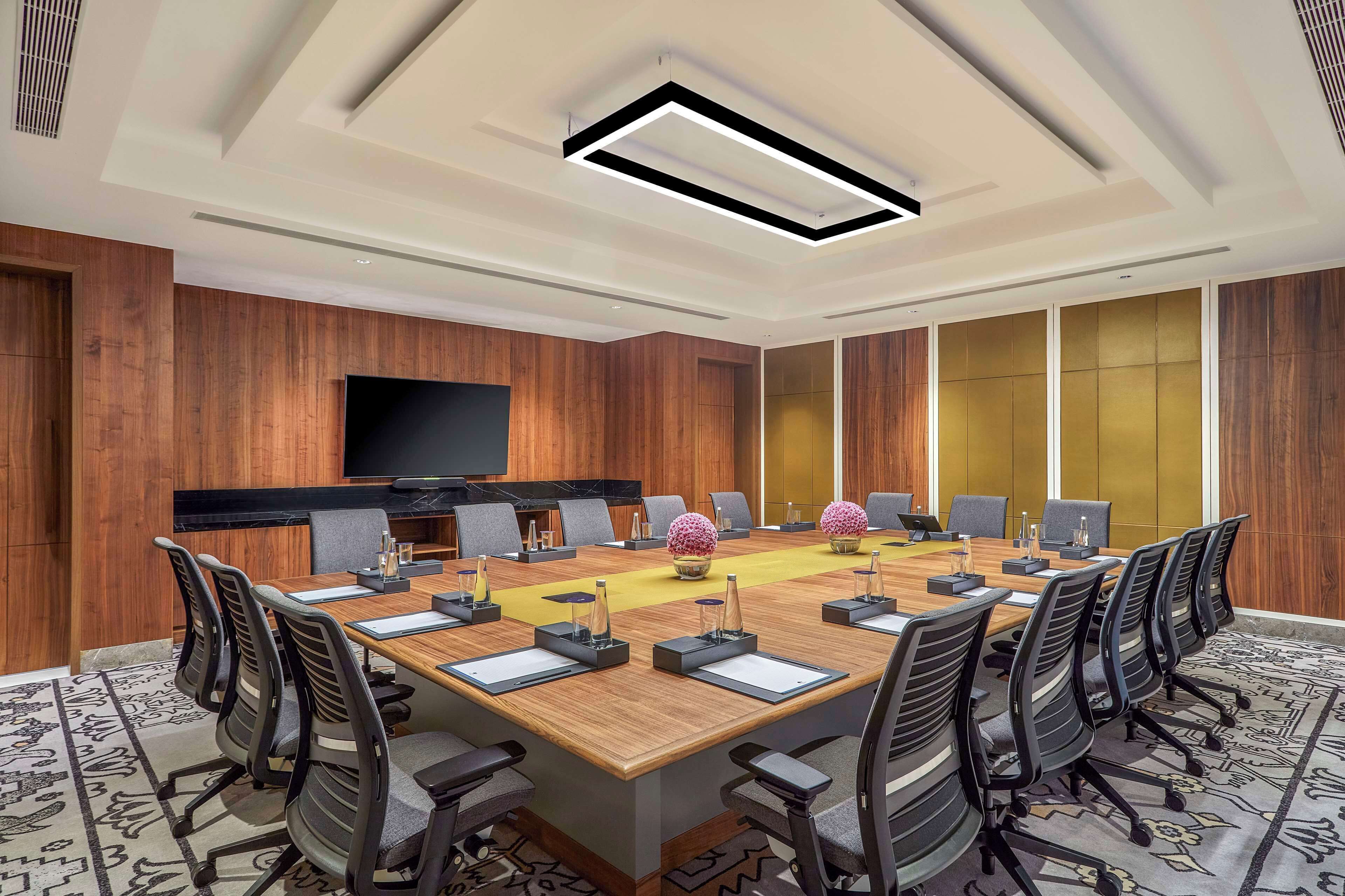 A conference room with a long table, multiple chairs, a flat-screen TV, and a decorative plant.