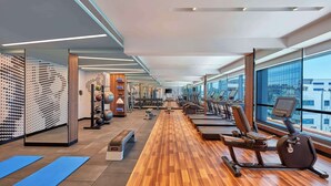 Un gimnasio moderno con equipo de ejercicio, suelo de madera y ventanas amplias con vistas a la ciudad.