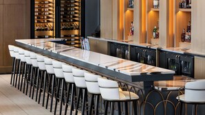 A modern bar area with a long counter, multiple stools, and a wine rack in the background. - Hilton BNA Nashville Airport Terminal (Nashville)