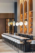 A modern bar area with a long counter, multiple stools, and a wine rack in the background.