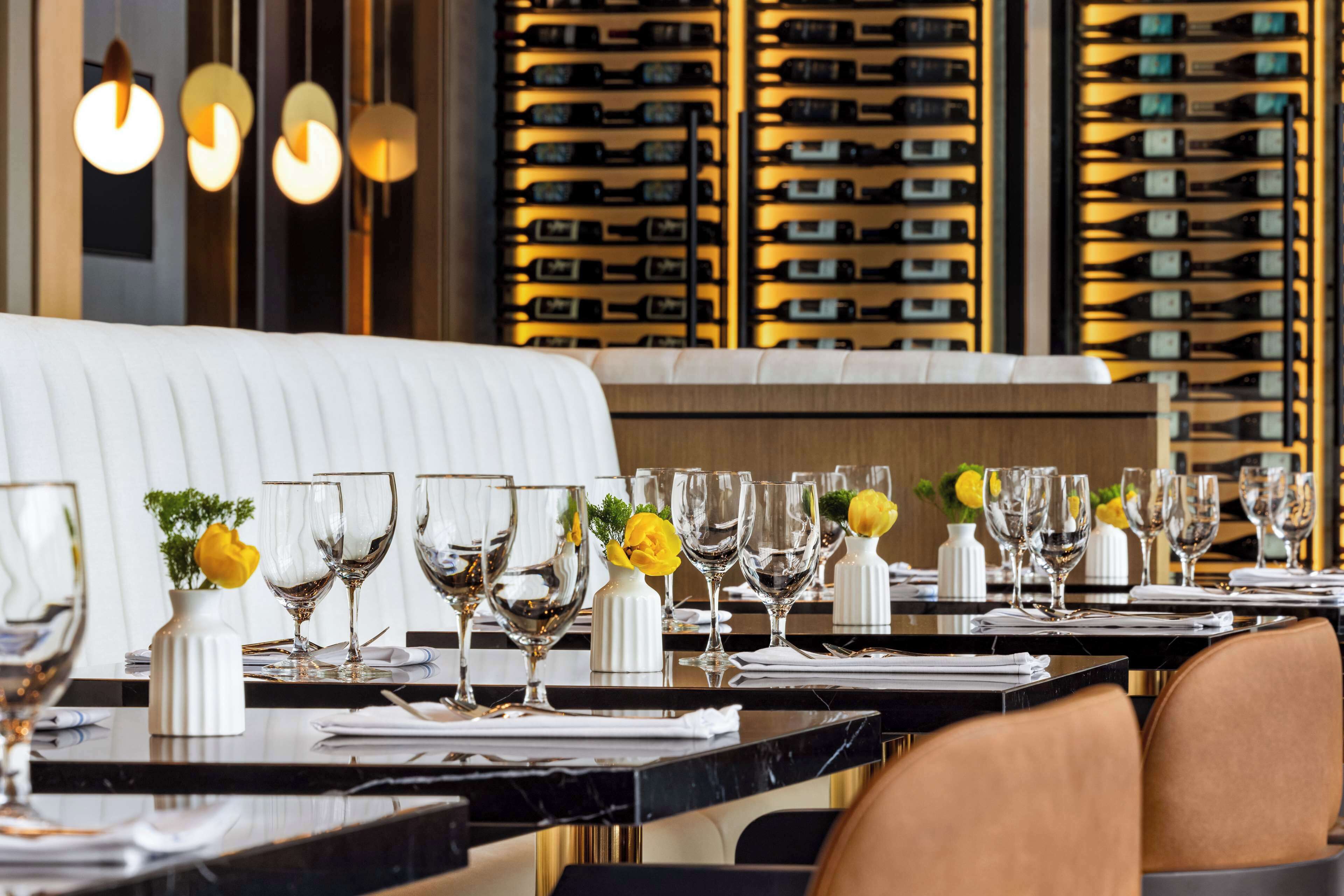 A restaurant setting with neatly arranged tables, wine racks in the background, and a plush seating area.