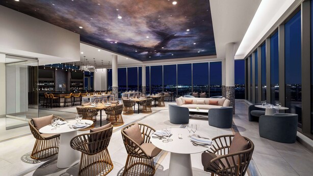 A modern rooftop lounge with round tables, wicker chairs, and a view of the city at night. - Hilton BNA Nashville Airport Terminal (Nashville)