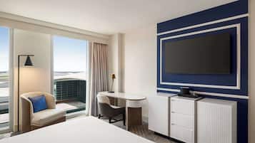 A hotel room with a large bed, a desk with a chair, a television mounted on the wall, and a view through the window.