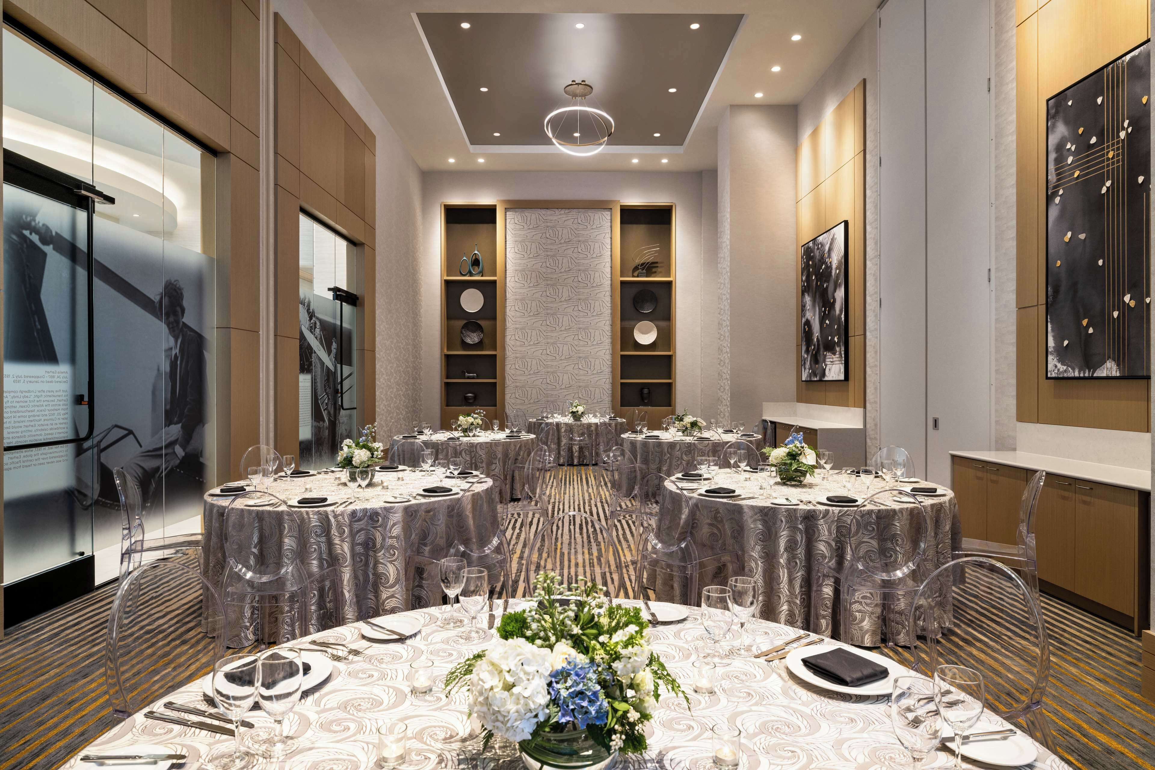 A conference room with round tables, clear chairs, and a central decorative plant.