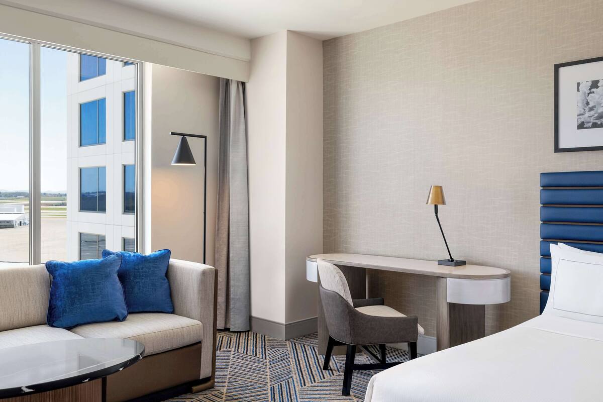A hotel room with a sofa, a desk, a chair, and a bed.