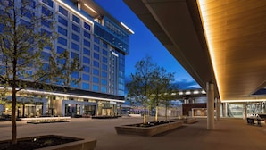 A modern hotel with a large glass facade, outdoor seating area, and a covered walkway. - Hilton BNA Nashville Airport Terminal (Nashville)