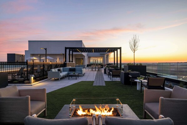 A modern outdoor patio with a fire pit, seating area, and a view of the city skyline at sunset.