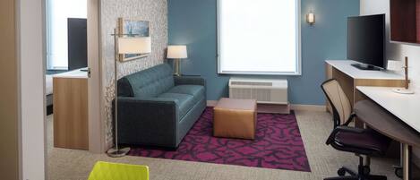 Quarto de hotel moderno com sofá, escrivaninha, televisão e janela com persianas.