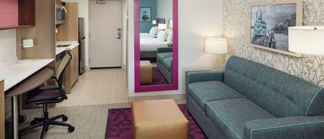 Une chambre d’hôtel équipée d’une kitchenette, d’un canapé, d’une petite table, d’un miroir et d’un lit.