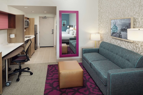 A hotel room with a kitchenette, a sofa, a small table, a mirror, and a bed.