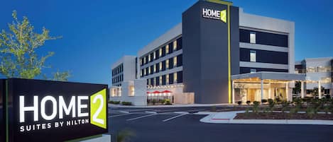 A modern hotel building with a sign reading "HOME 2 SUITES BY HILTON".