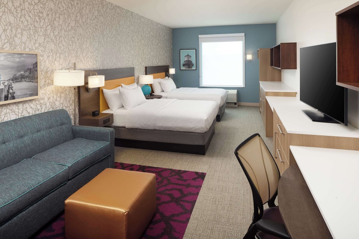 A hotel room with two beds, a sofa, a desk, and a TV.