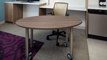 A modern office space with a round table, office chairs, a desk with a computer, and a coffee machine.