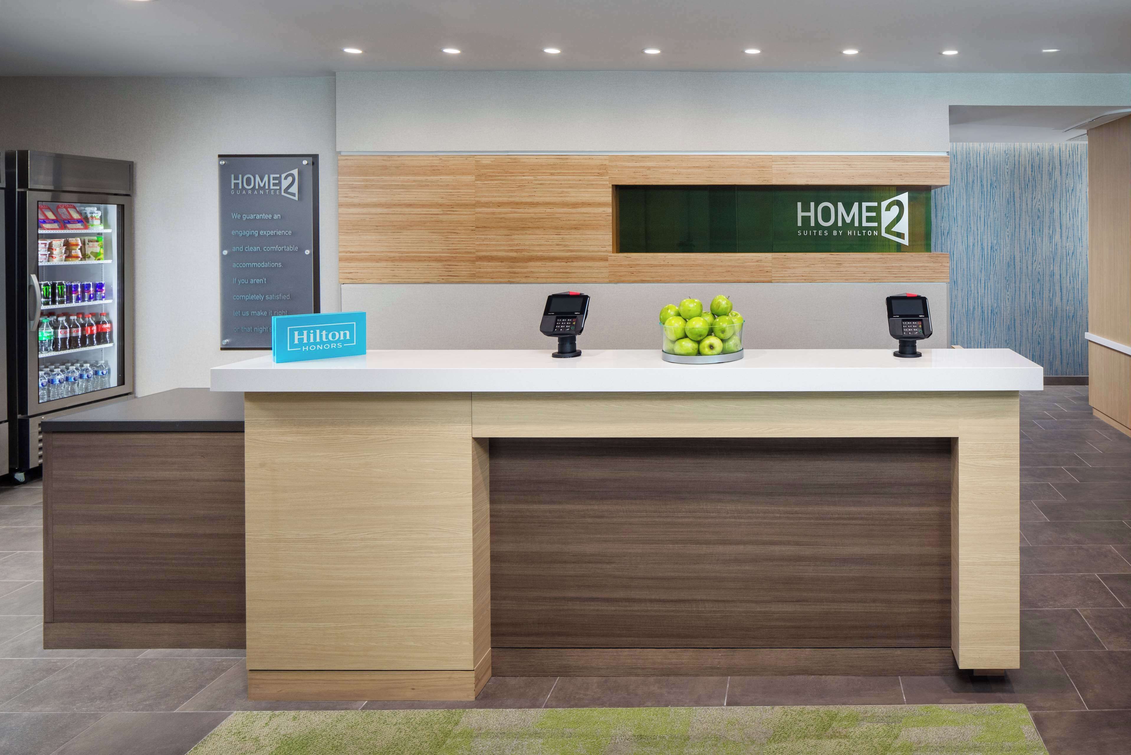 A modern hotel reception desk with a digital display, a minibar, and a sign indicating Hilton Honors.