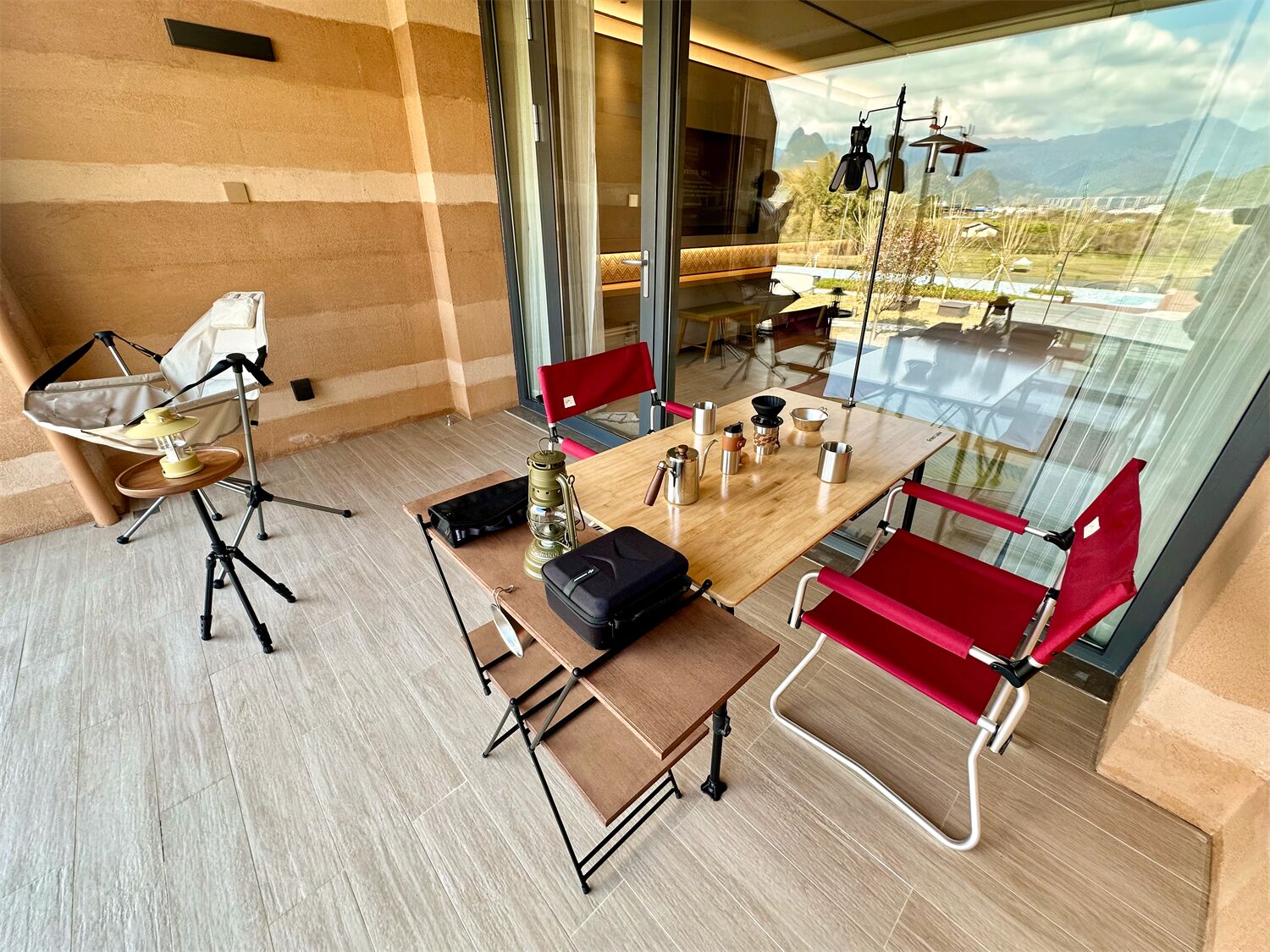 Ein modernes Zimmer mit einem Holztisch, roten Stühlen, einem Campingstuhl und Bergblick durch große Fenster.