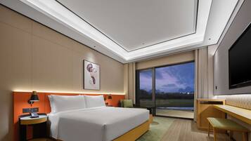 A modern hotel room with a large bed, a desk, a TV, and a view of the outdoors.