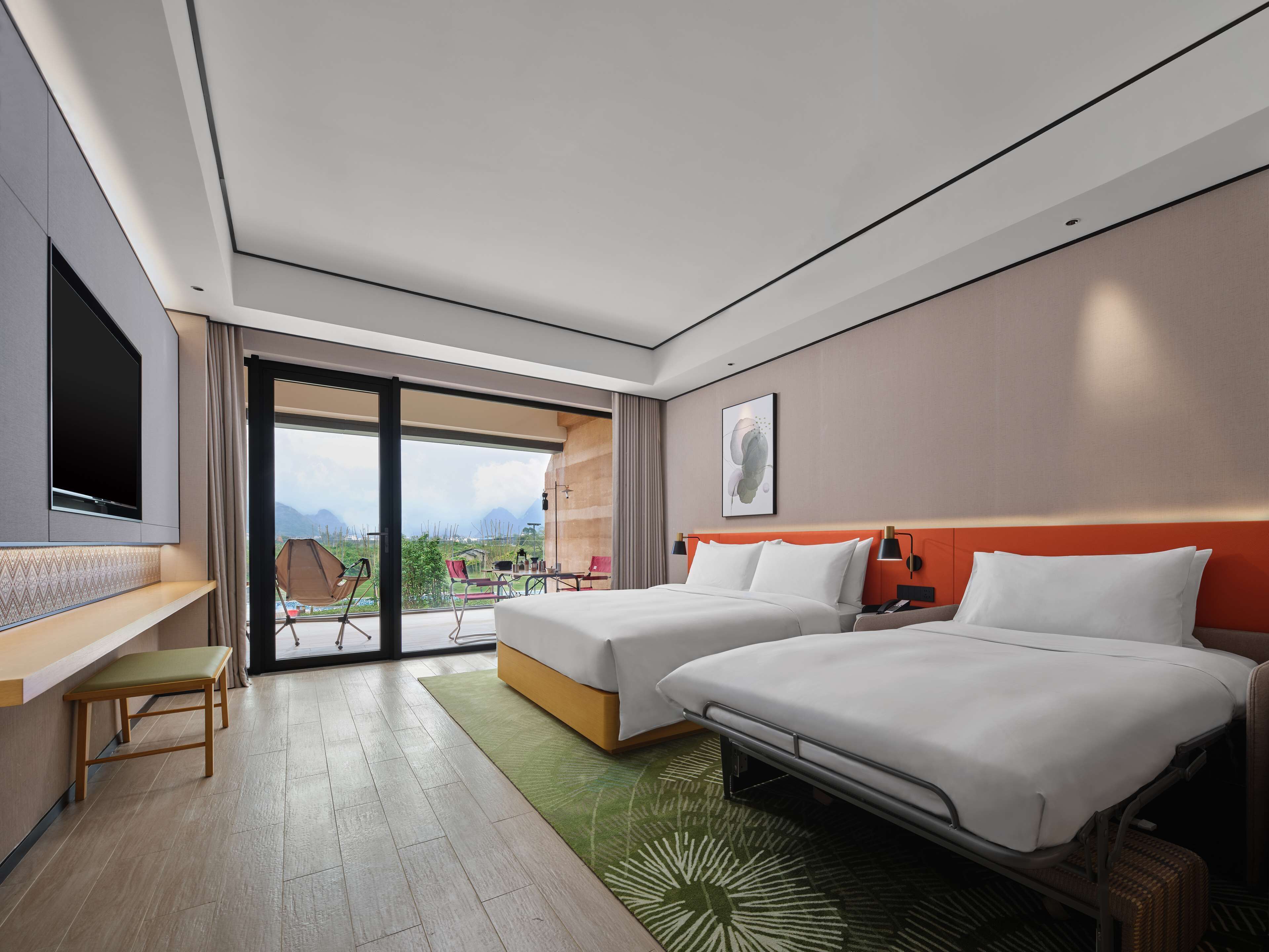 A modern hotel room with two beds, a TV, a desk, and a balcony with a view of the mountains.