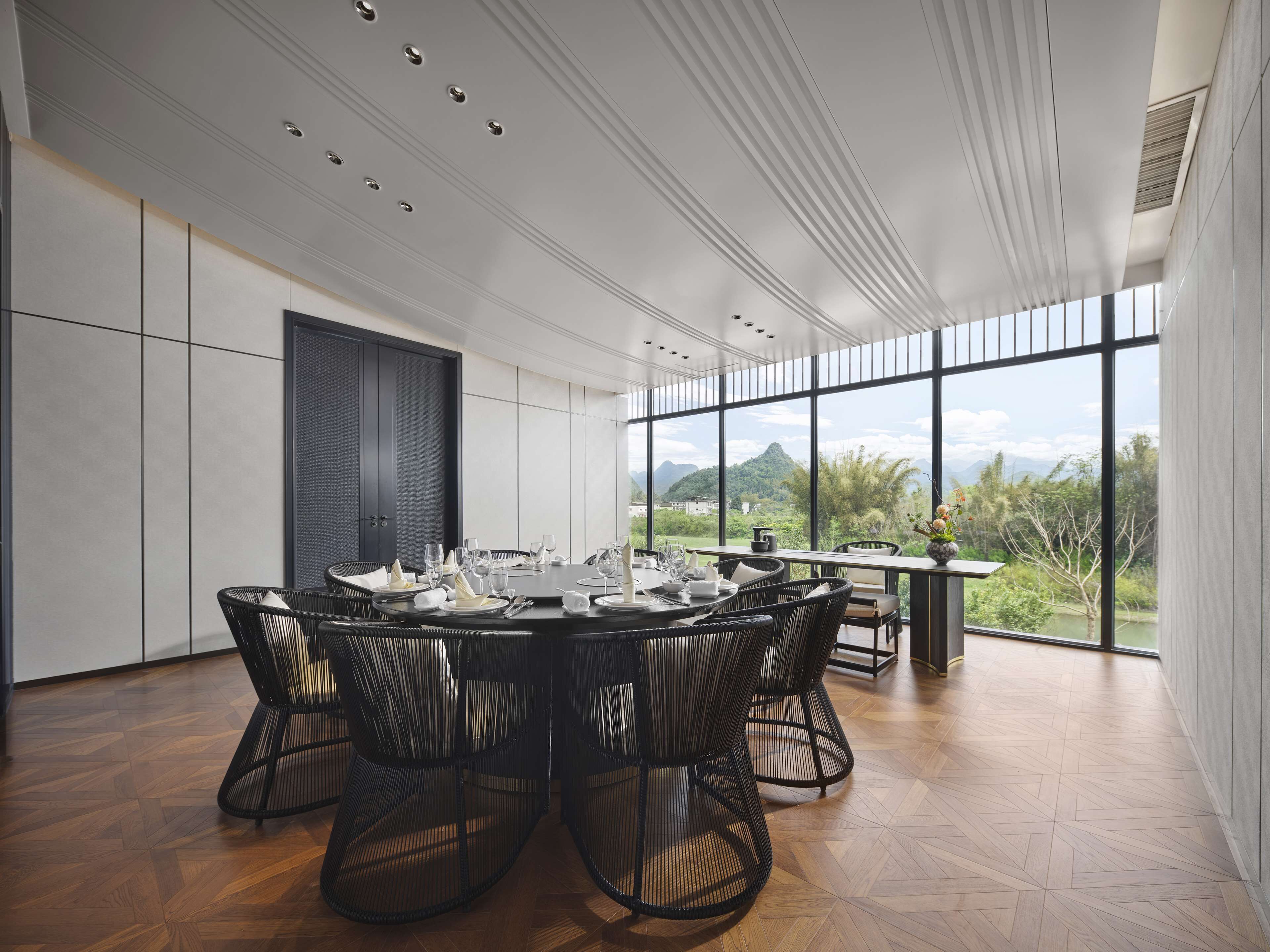 Un espace repas moderne avec une table ronde, des chaises noires et une vue sur les montagnes grâce à de grandes fenêtres.