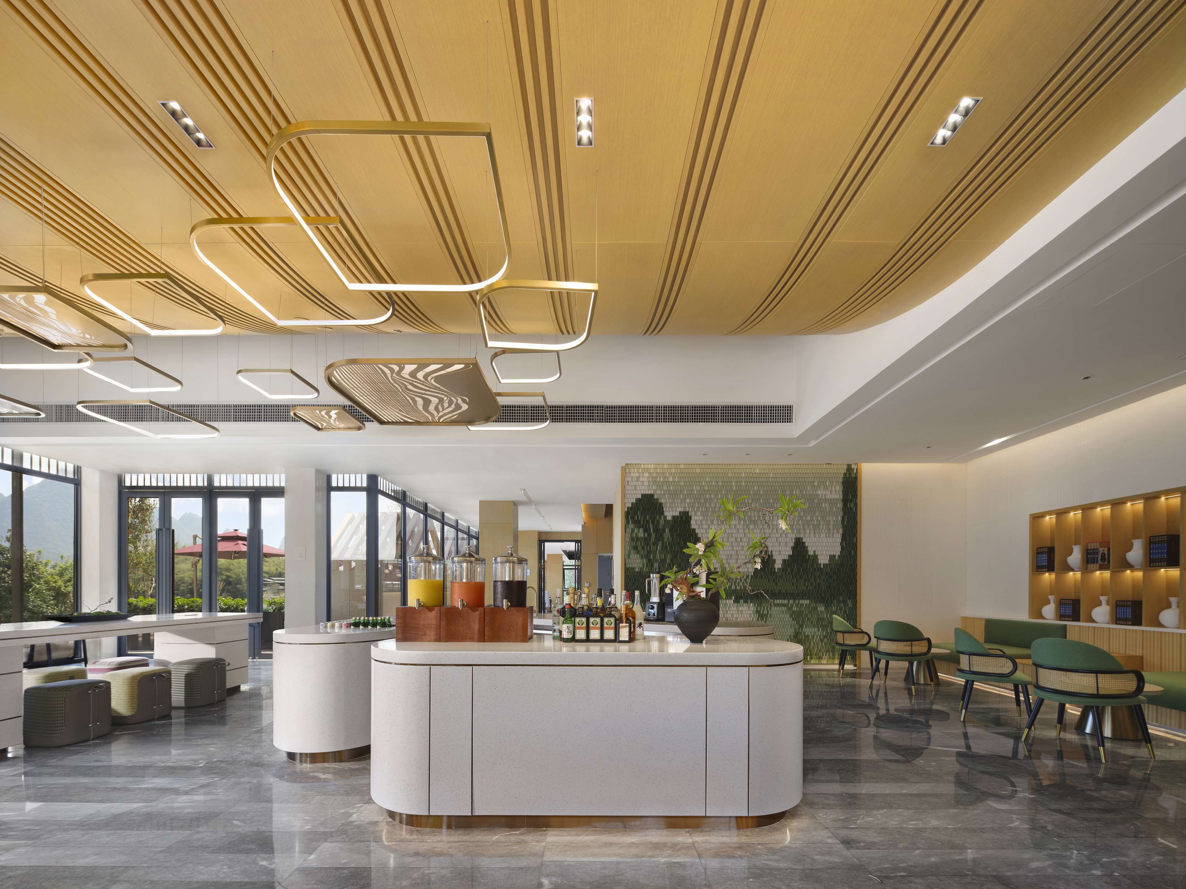 A modern hotel lobby with a central reception desk, seating area, and large windows offering views of greenery.