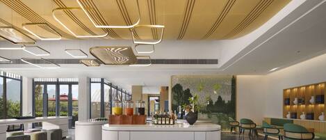 A modern hotel lobby with a central reception desk, seating area, and large windows offering views of greenery.