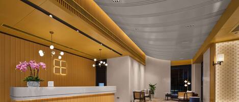 Un área de recepción moderna con un mostrador de madera, un espacio de espera con sillas y una mesa, y un suelo con diseño.