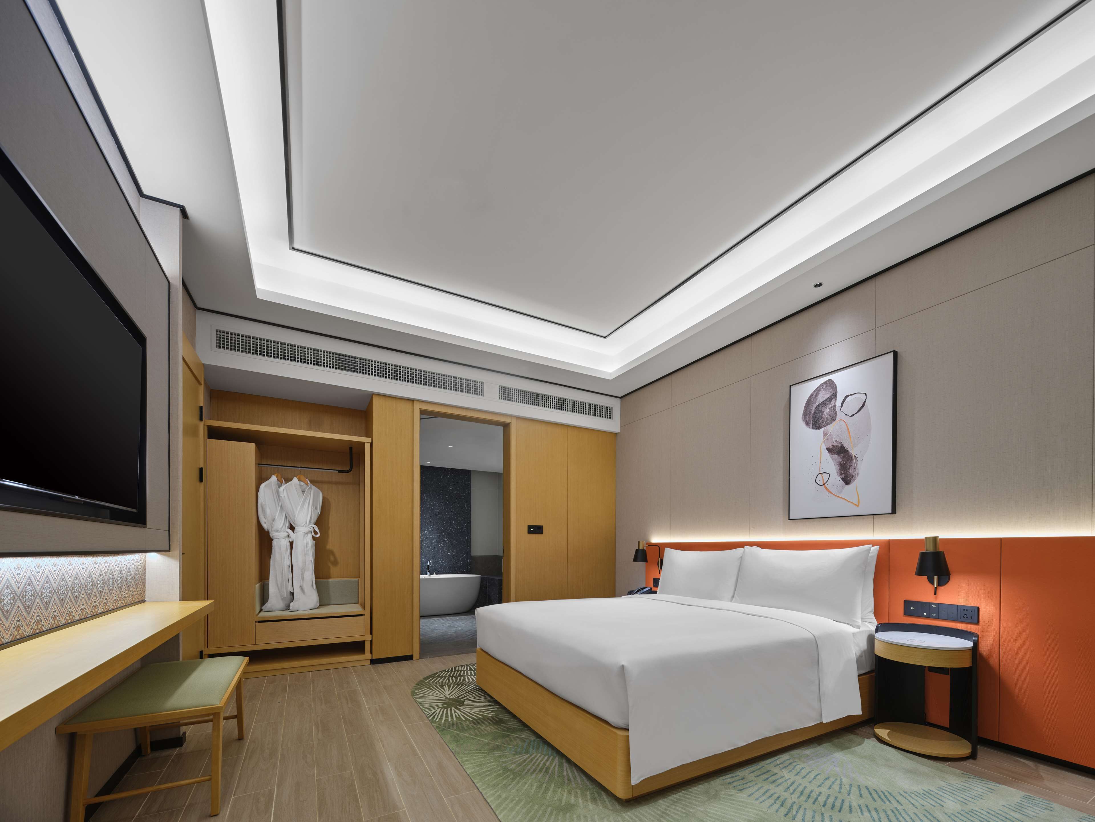 A modern hotel room with a large bed, a seating area, a walk-in closet, a bathroom with a bathtub, and a flat-screen TV.