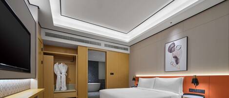 A modern hotel room with a large bed, a seating area, a walk-in closet, a bathroom with a bathtub, and a flat-screen TV.