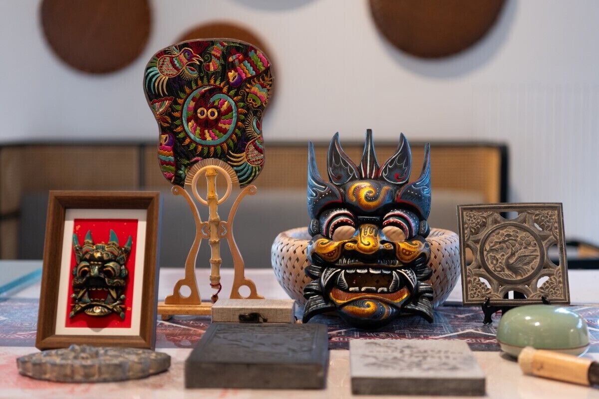 A table with various cultural artifacts including a framed mask, a decorative headpiece, a carved wooden figure, and a jade stone.
