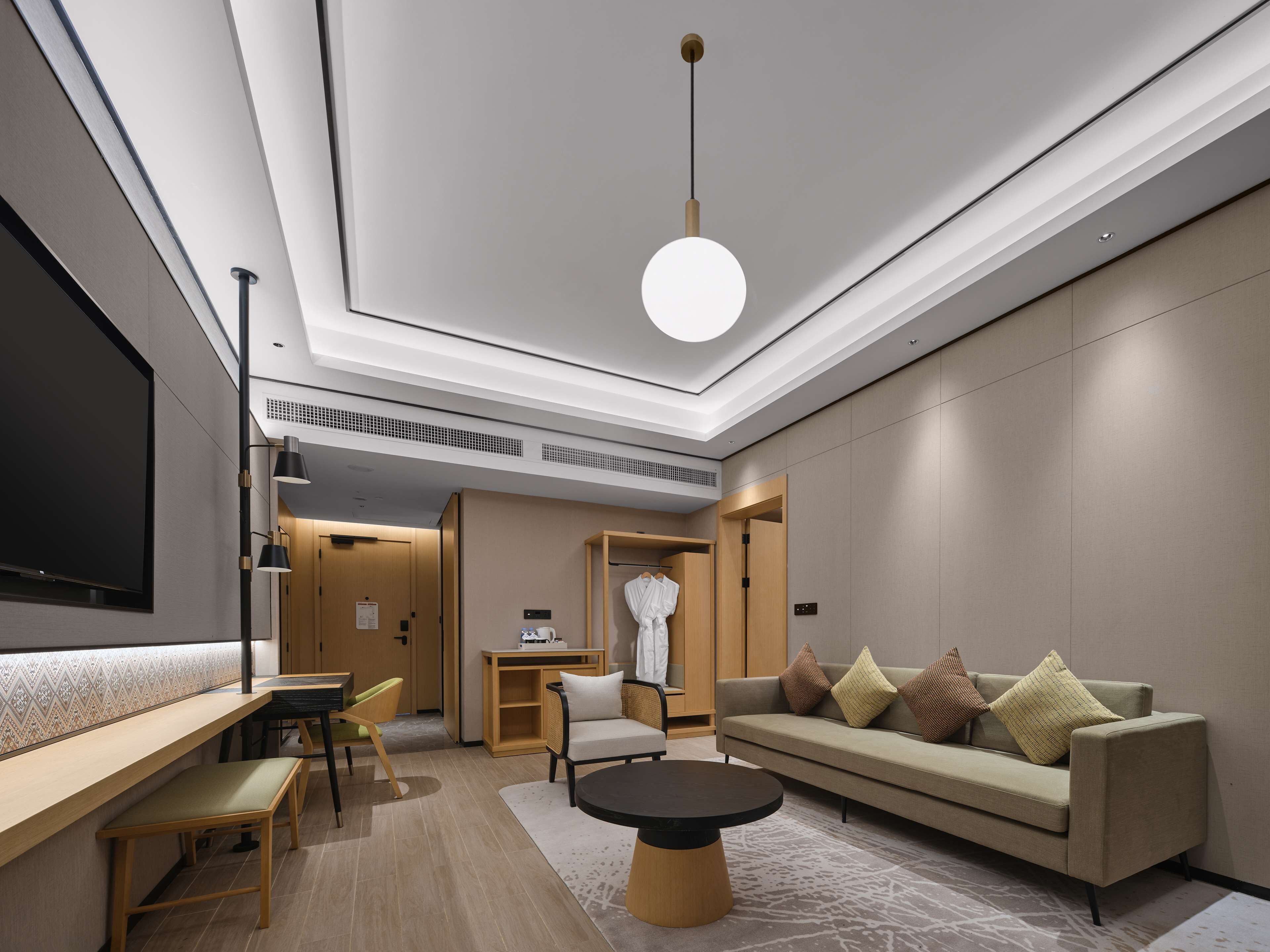 Una habitación de hotel moderna con sofá, una mesa de comedor, sillas, televisión e iluminación en el techo.