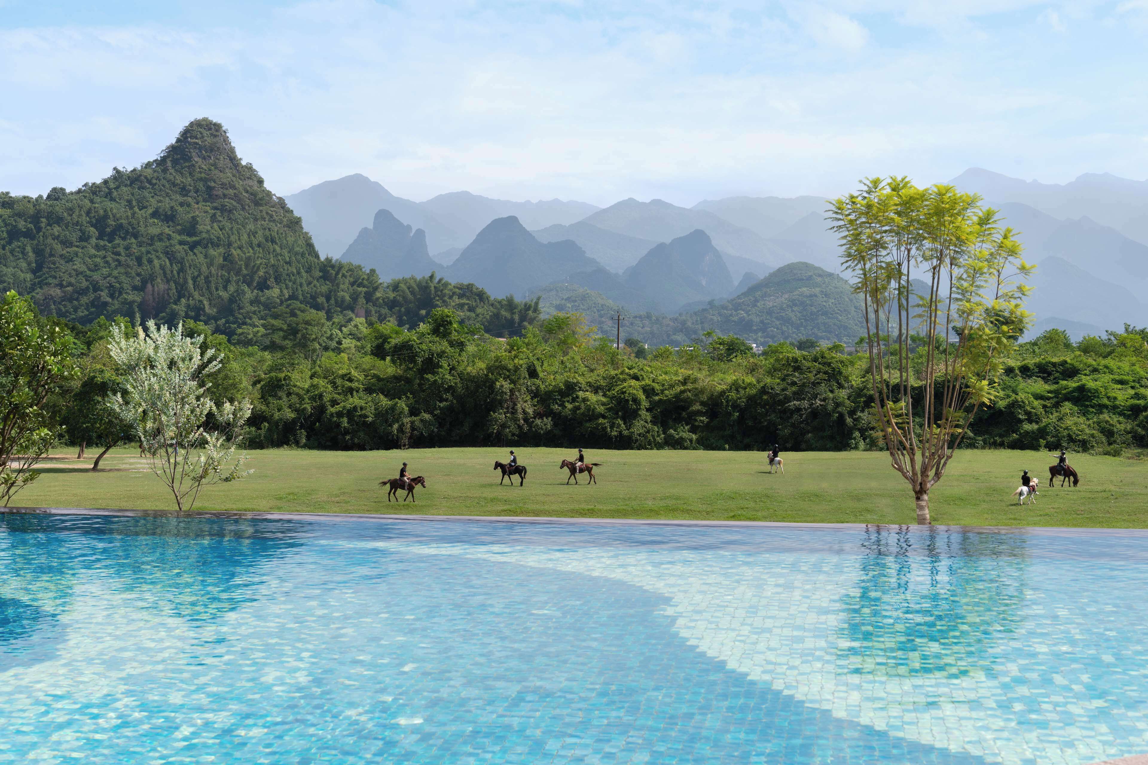 A pool with clear blue water, surrounded by lush greenery and distant mountains.