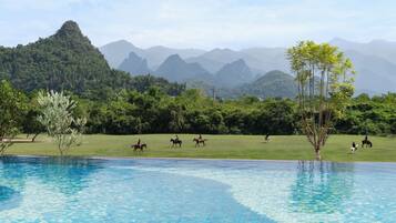 A pool with clear blue water, surrounded by lush greenery and distant mountains.