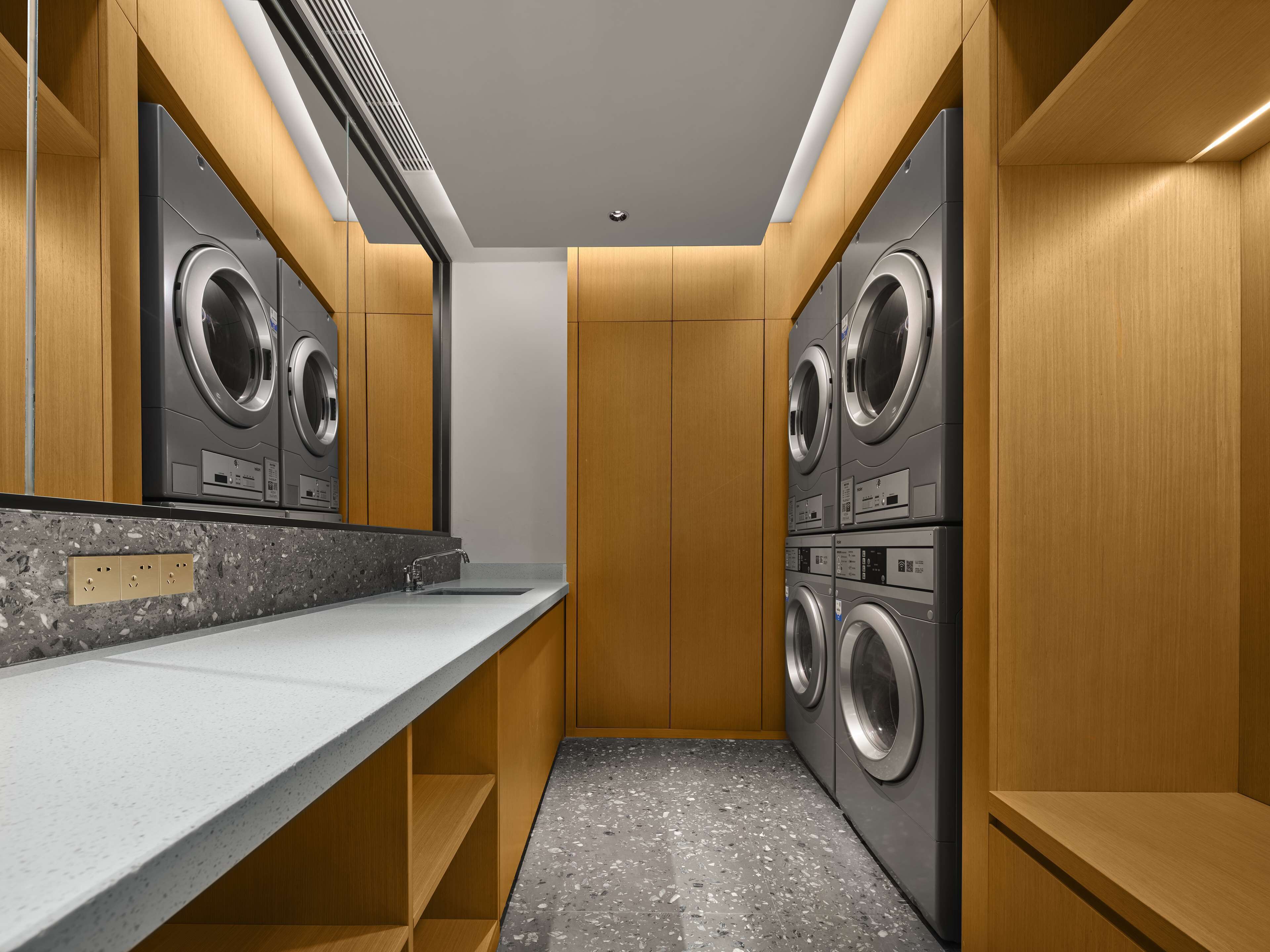 A laundry room with two stacked front-loading washing machines, a granite countertop, and wooden cabinetry.