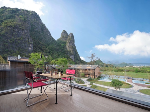 A dining area with a table and chairs, overlooking a mountainous landscape with a view of a bridge and a body of water.