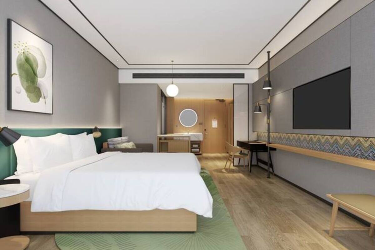 A modern hotel room with a large bed, a desk, a vanity, and a television.
