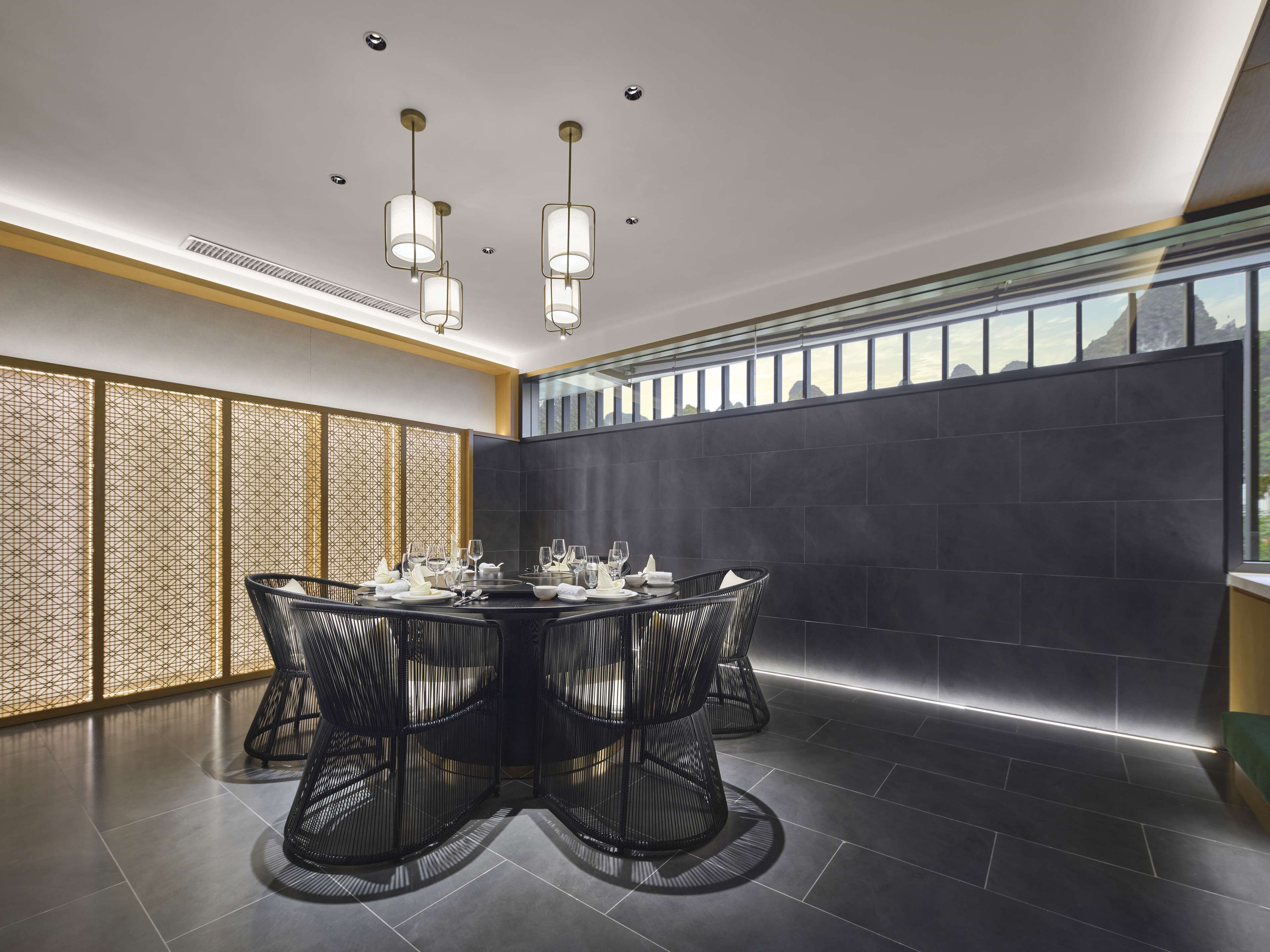 A modern dining area with a round table set for four, black woven chairs, and a dark tiled wall.