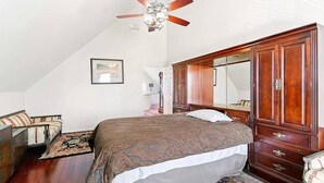 Un dormitorio con una cama grande, un armario de madera, un ventilador de techo y un cuadro en la pared.
