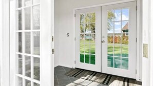 Una puerta blanca con un panel de vidrio, un felpudo a rayas negras y blancas, y vistas de un césped verde y árboles.