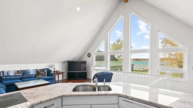 Una cocina moderna con una isla grande, un comedor con sofá azul y vistas a un lago a través de amplios ventanales.