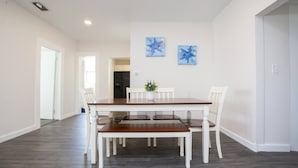 Ein Esszimmer mit Holztisch und weißen Stühlen, im Hintergrund eine Küche sowie zwei blaue Wandbilder mit Seesternen.